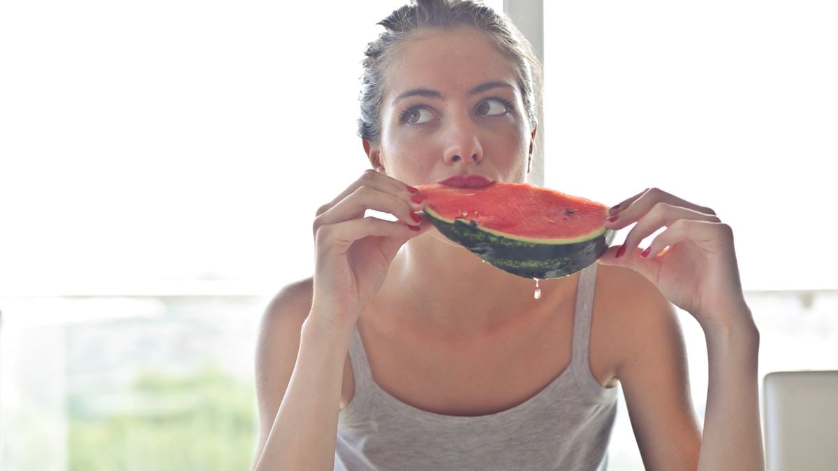 Portrait of a woman eating watermelon indoors, reflecting health and summer vibes.